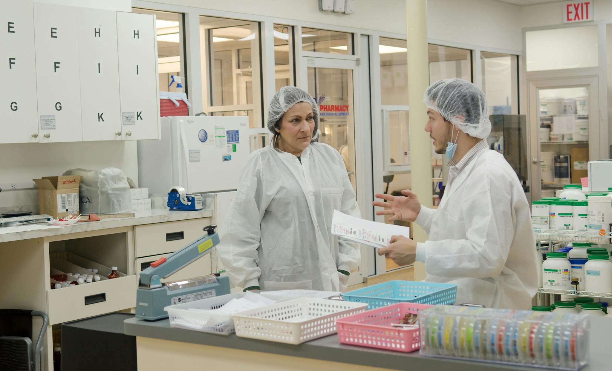 Concentrated laboratory workers wearing white robes and hats standing with papers in contemporary chemical room and discussing results of scientific research